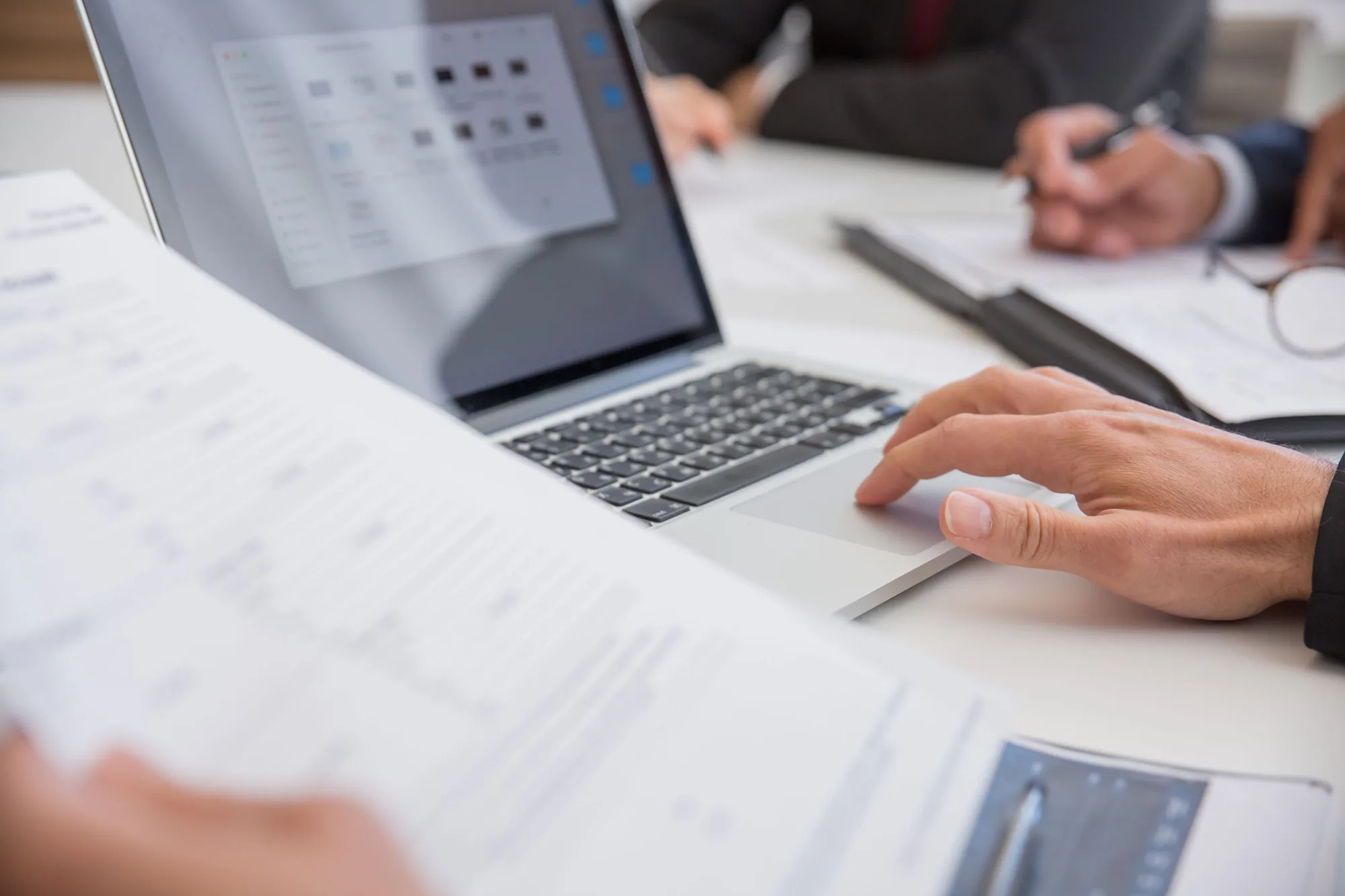 Hands working through printed documents next to a laptop on an office desk