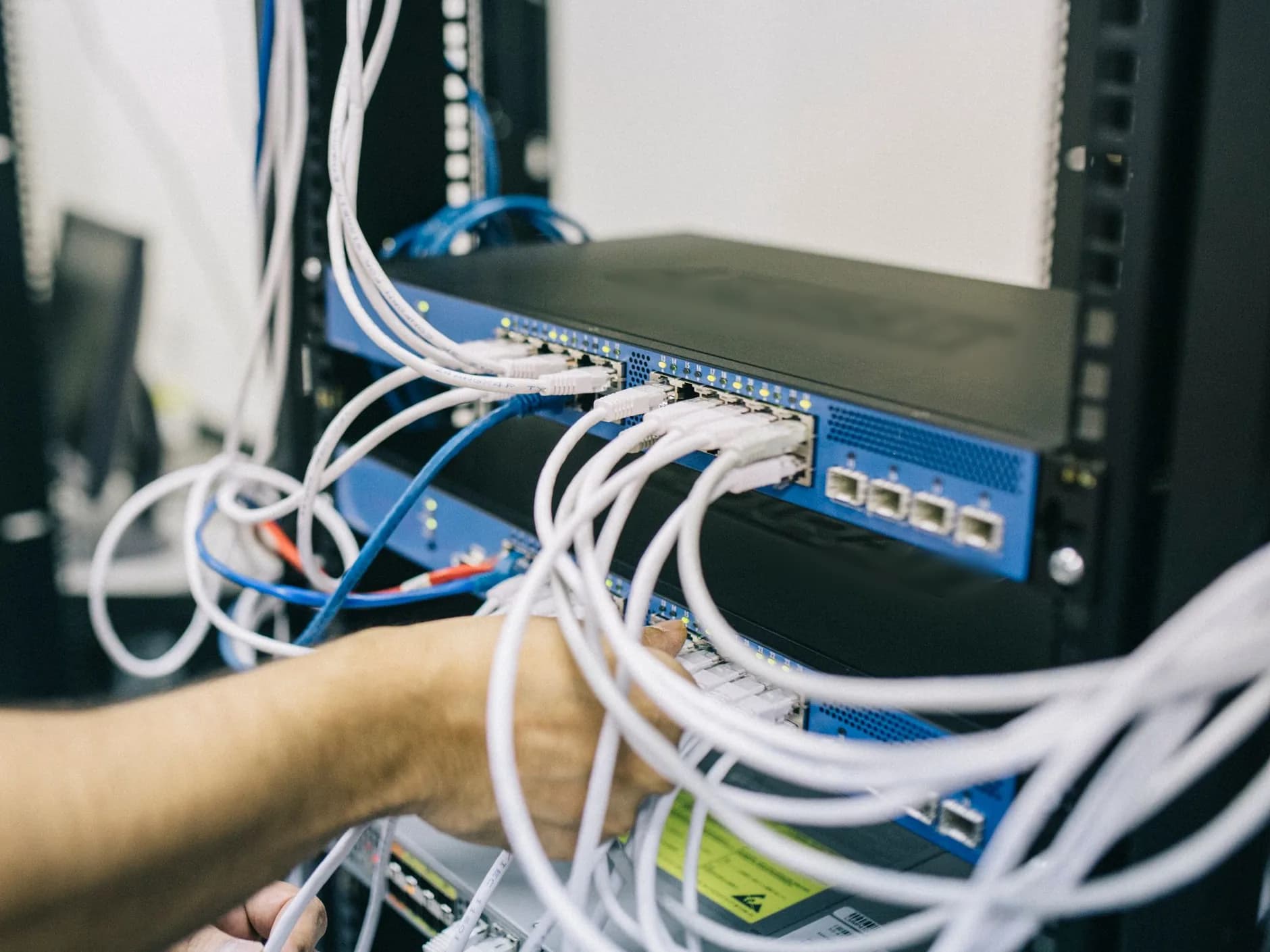 Technician's hand plugging network cables into a rack-mounted switch